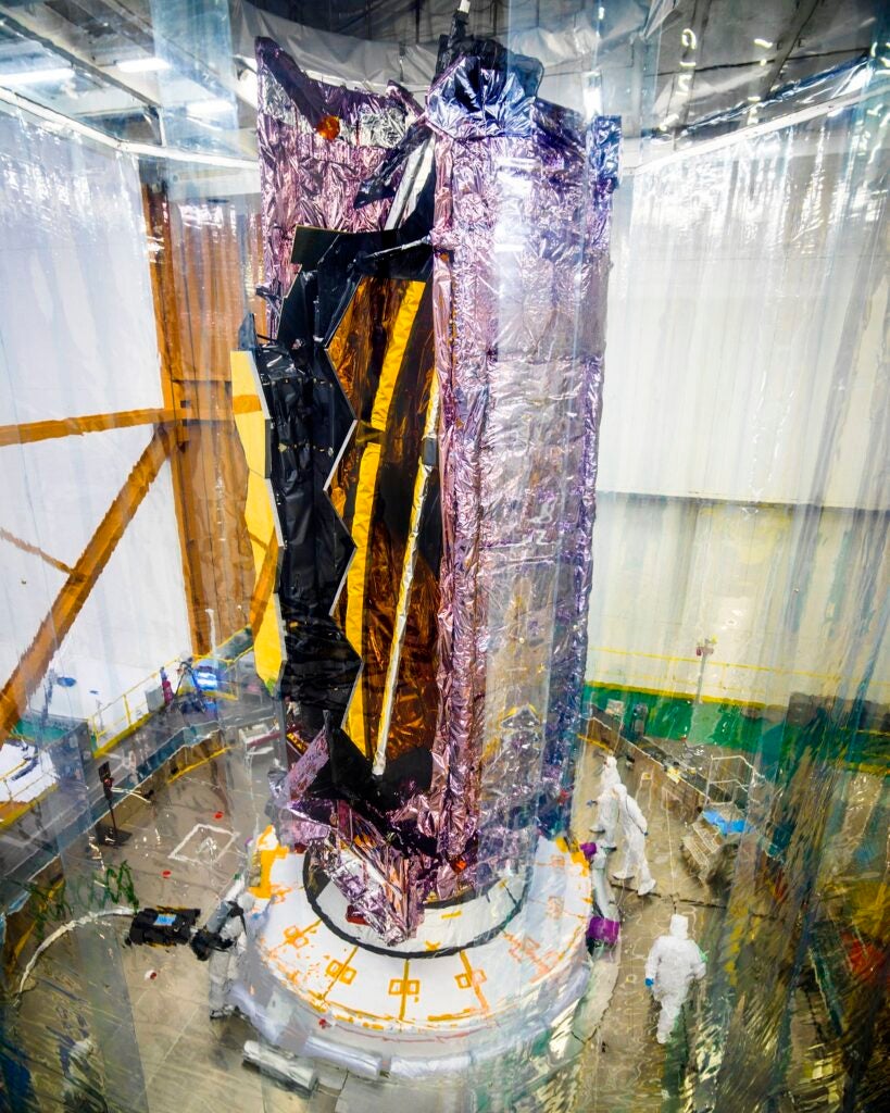 James Webb Space Telescope folded up in a cylinder on a vertical platform surrounded by a plastic cover